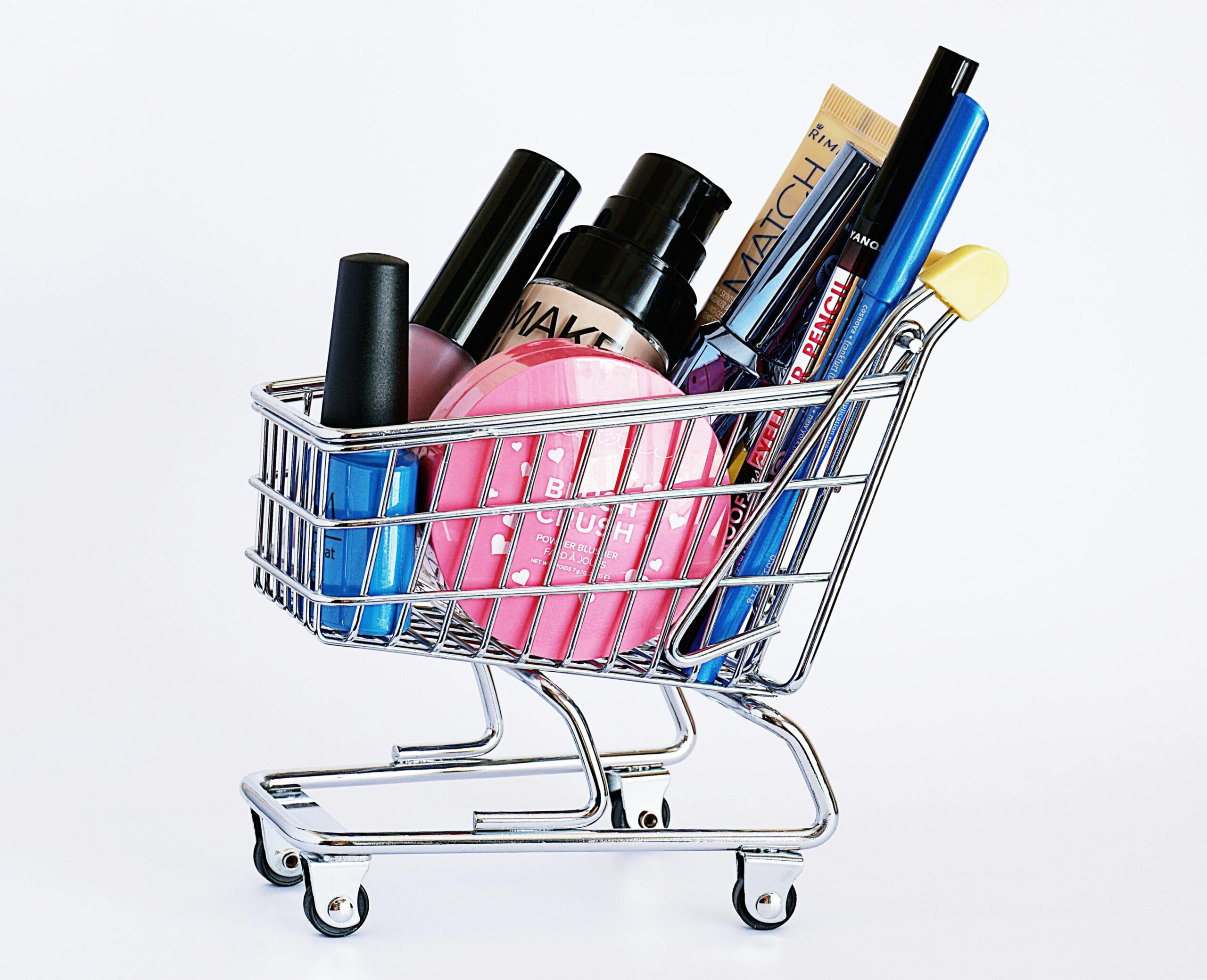 Home Miniature shopping cart filled with a variety of cosmetics on a white background.